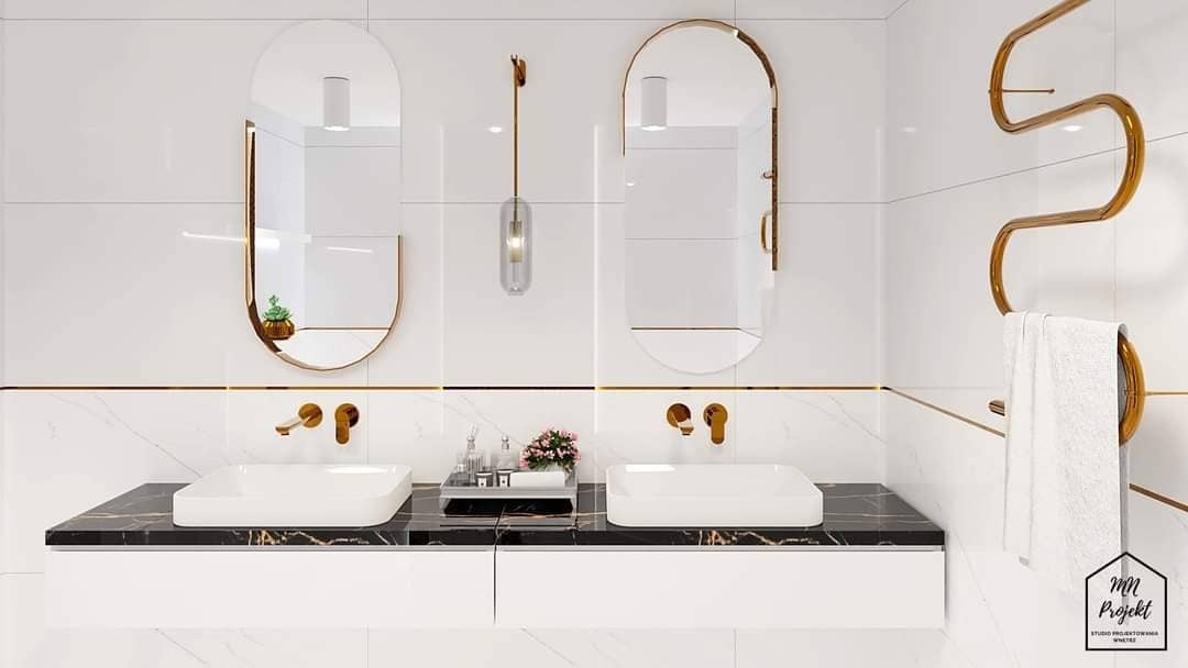 Elegancka łazienka z dwoma umywalkami nablatowymi, czarnym blatem imitującym marmur, owalnymi lustrami w złotej ramie, grzejnikiem drabinkowym w kolorze złota i białymi płytkami z marmurkowym wzorem.