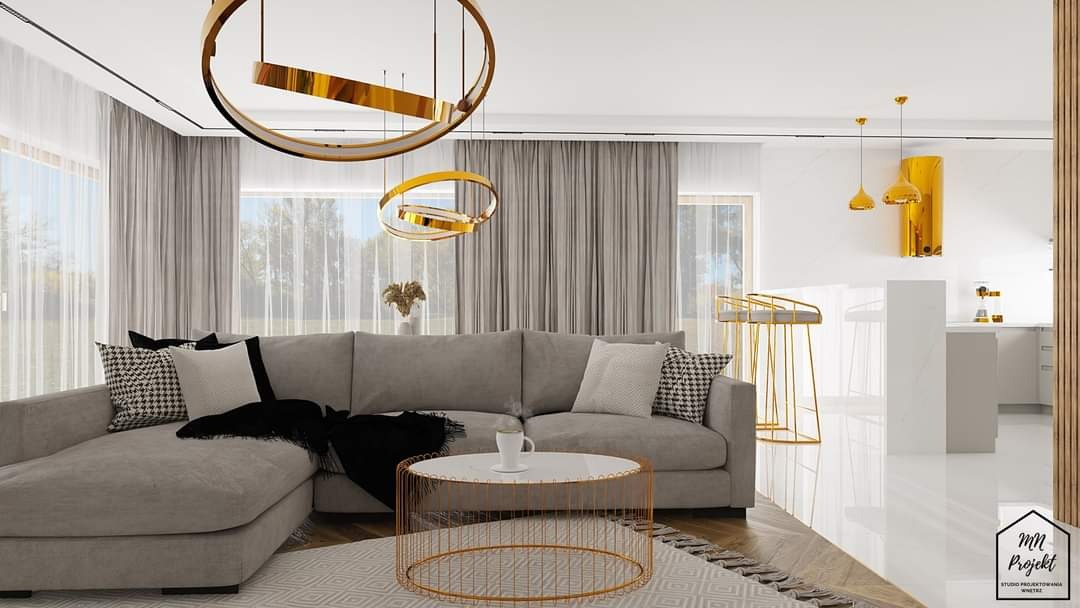 Salon w odcieniach szarości i złota z narożną sofą, okrągłym stolikiem kawowym z filiżanką i wiszącymi lampami w kształcie złotych pierścieni.