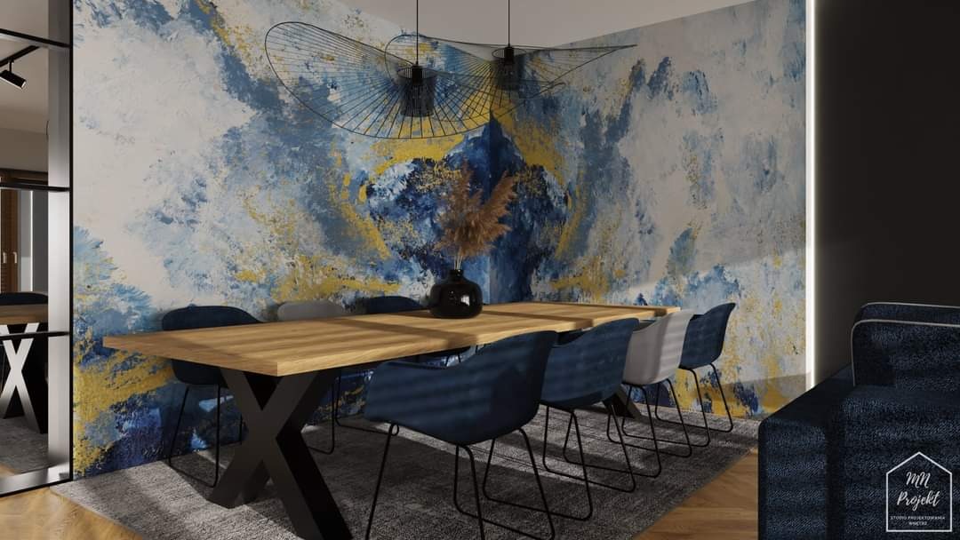 Nowoczesna jadalnia z drewnianym stołem na metalowych nogach w kształcie litery X, krzesłami obitymi granatowym aksamitem i abstrakcyjną tapetą w odcieniach błękitu, złota i bieli.