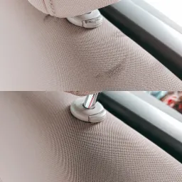 Porównanie przed i po: tapicerka samochodowa w jasnym odcieniu beżu, z widocznym zabrudzeniem na górnej części zdjęcia i czystą powierzchnią na dole, uchwyt zagłówka i fragment ramy okna widoczne...