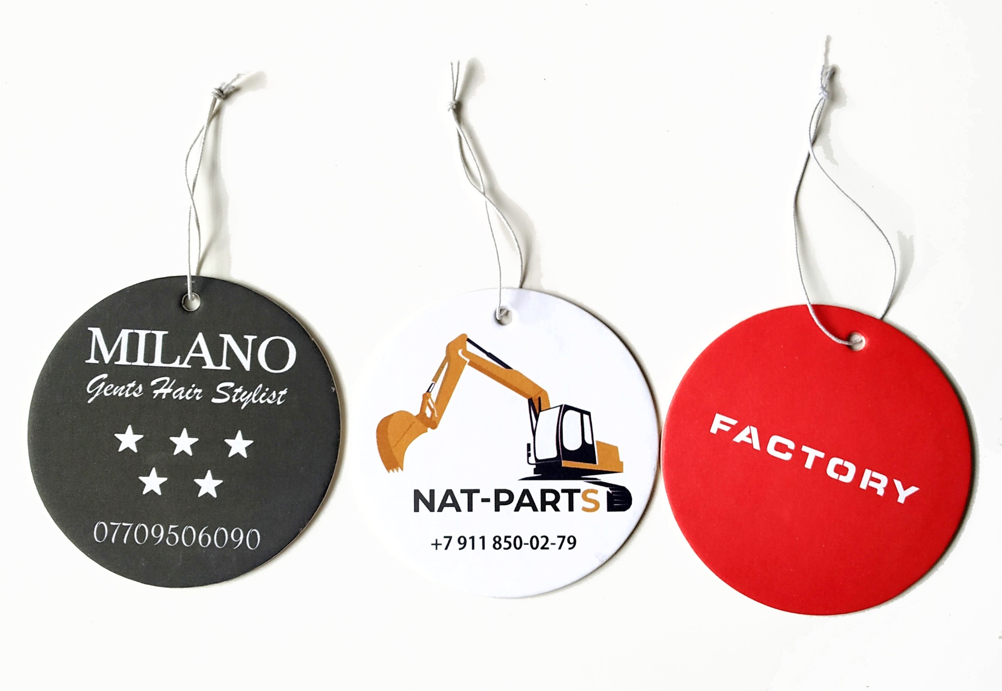 Trzy okrągłe zawieszki z różnymi nadrukami: fryzjer, części maszyn i fabryka, zawieszone na sznurkach na białym tle.