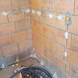 Wewnętrzne ściany z pustaków ceramicznych z widoczną instalacją elektryczną w postaci białych przewodów i pomarańczowych puszek, częściowo zamaskowanych gipsem.