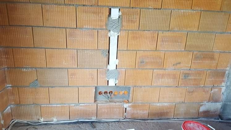 Wykuta bruzda w ścianie z cegły ceramicznej, w której umieszczono peszel instalacyjny; widoczne ślady zaprawy murarskiej i wystające przewody. Otwór pod gniazdka RTV.