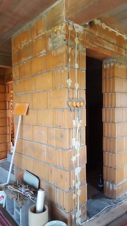 Wewnętrzne okablowanie elektryczne w nowym budynku z cegły, widoczne puszki instalacyjne i przewody zabezpieczone gipsem.