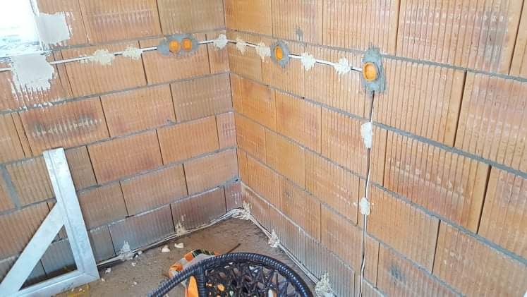 Wewnętrzne ściany z pustaków ceramicznych z widoczną instalacją elektryczną w postaci białych przewodów i pomarańczowych puszek, częściowo zamaskowanych gipsem.