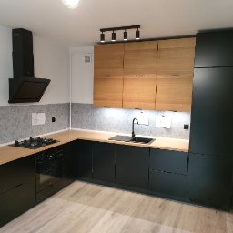 Teoria Wnętrza Aleksandra Koter - Nowoczesna kuchnia z czarnymi szafkami dolnymi i drewnianymi górnymi, oświetlenie punktowe, szara ściana nad blatem.