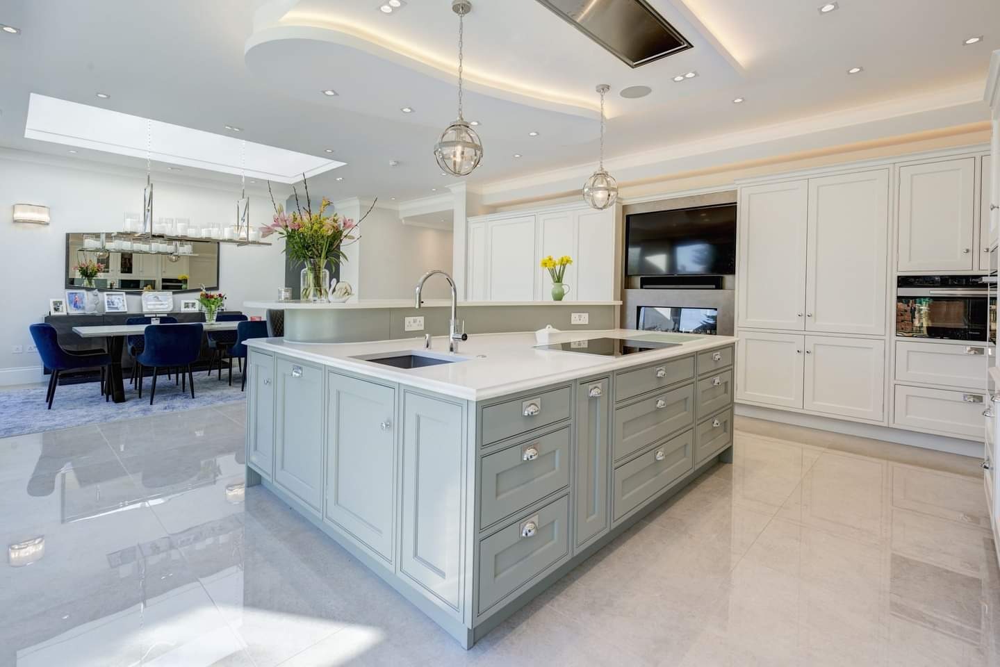 Jasna, przestronna kuchnia z wyspą w Lublinie, szare szafki z frezowanymi frontami, biały blat, widok na jadalnię z niebieskimi krzesłami i lustrem.