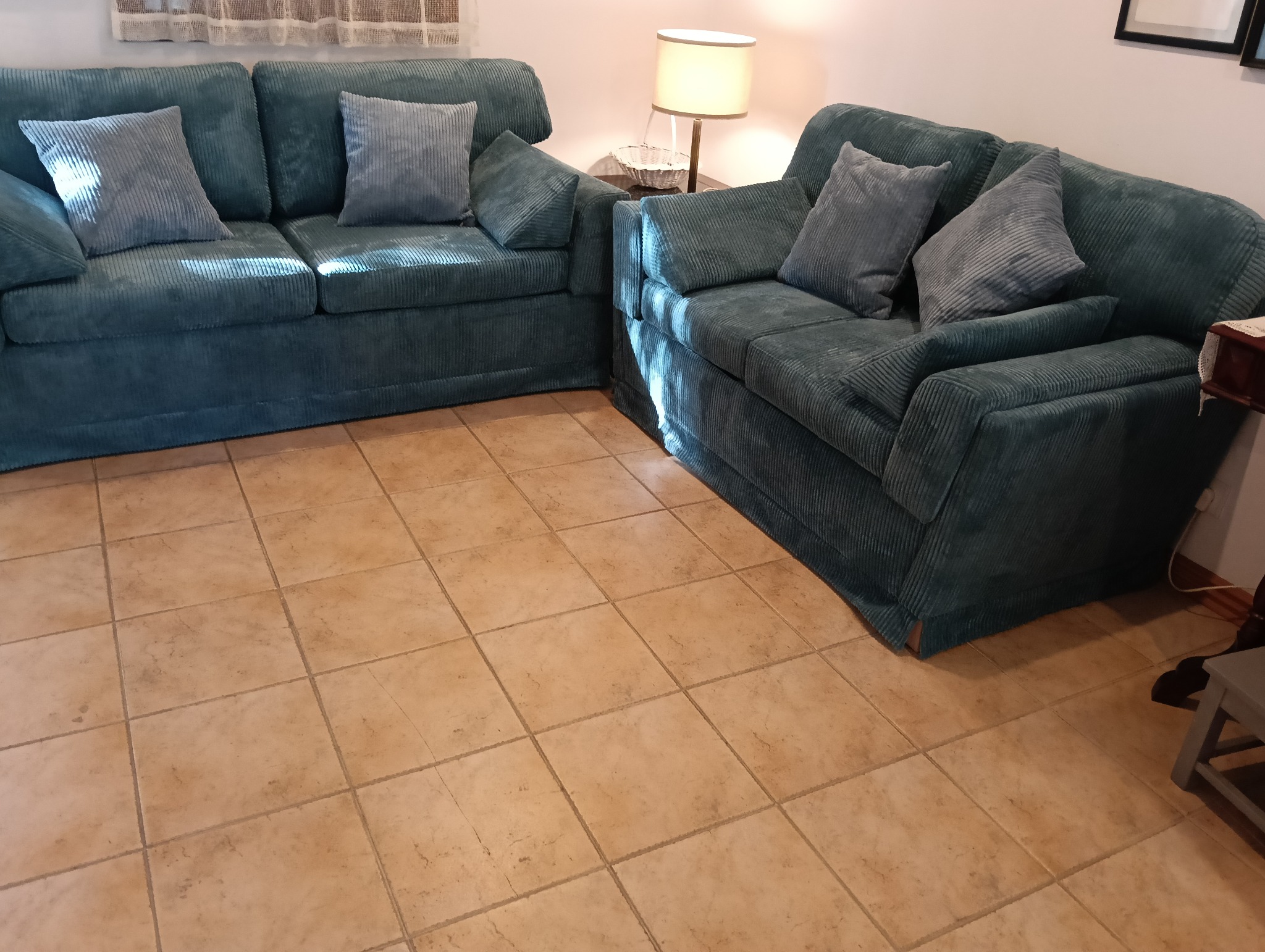 Komplet wypoczynkowy: sofa dwuosobowa i fotel w odcieniach zieleni, z poduszkami w paski, na tle jasnych płytek podłogowych i lampy.