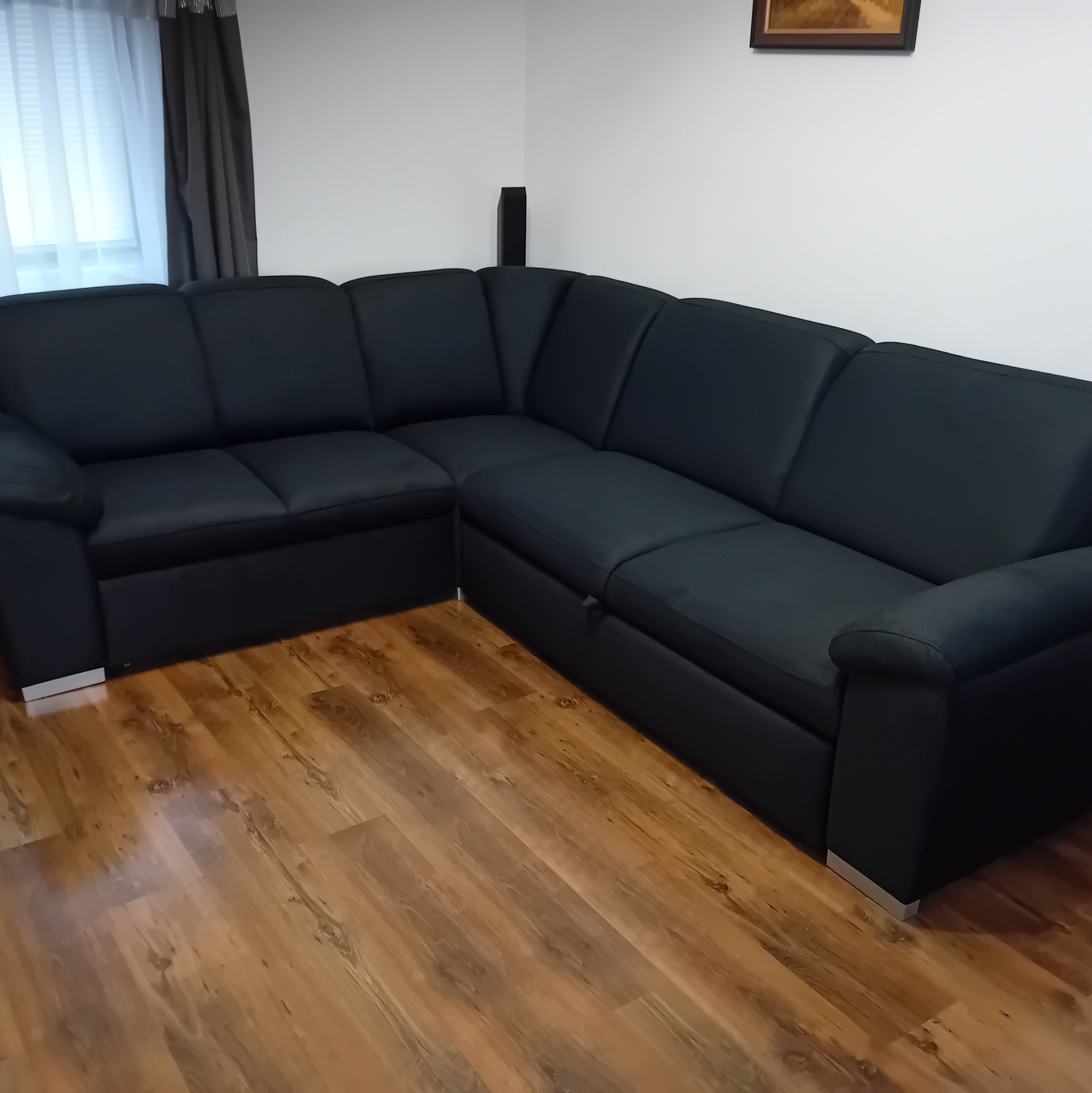 Czarny narożnik z poduszkami i metalowymi nóżkami na drewnianej podłodze. Minimalistyczny design w salonie w Krakowie. Nowoczesny mebel.