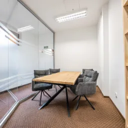 Klimatyczne biuro z drewnianym stołem i szarymi krzesłami, przeszklona ściana z poziomymi pasami, regał z książkami prawniczymi w tle.