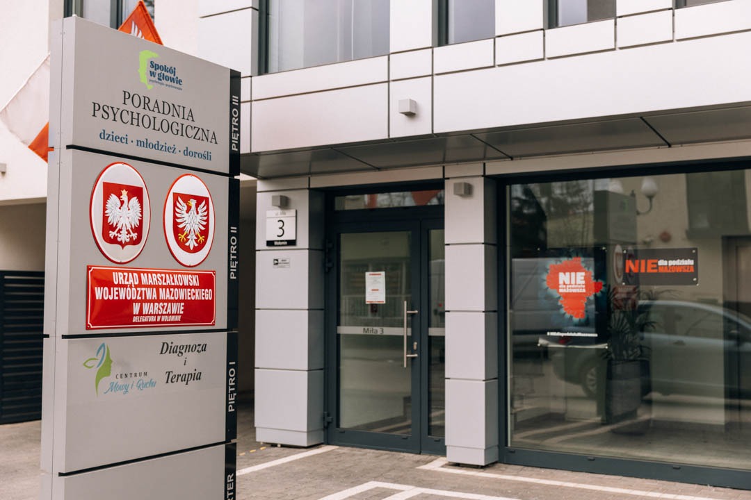Wejście do poradni psychologicznej z szyldem informacyjnym, widoczne logo 'Spokój w głowie', godło Polski, adres Mila 3, oraz informacja o Urzędzie Marszałkowskim Województwa Mazowieckiego.