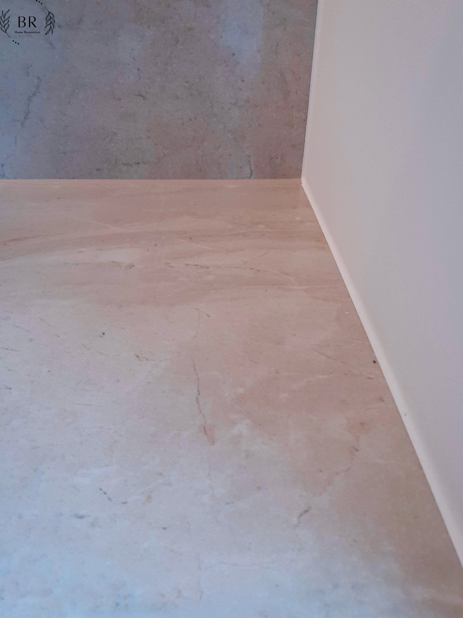 Fragment wykończonej łazienki z beżową marmurową podłogą i szarą ścianą, widoczna biała listwa przypodłogowa