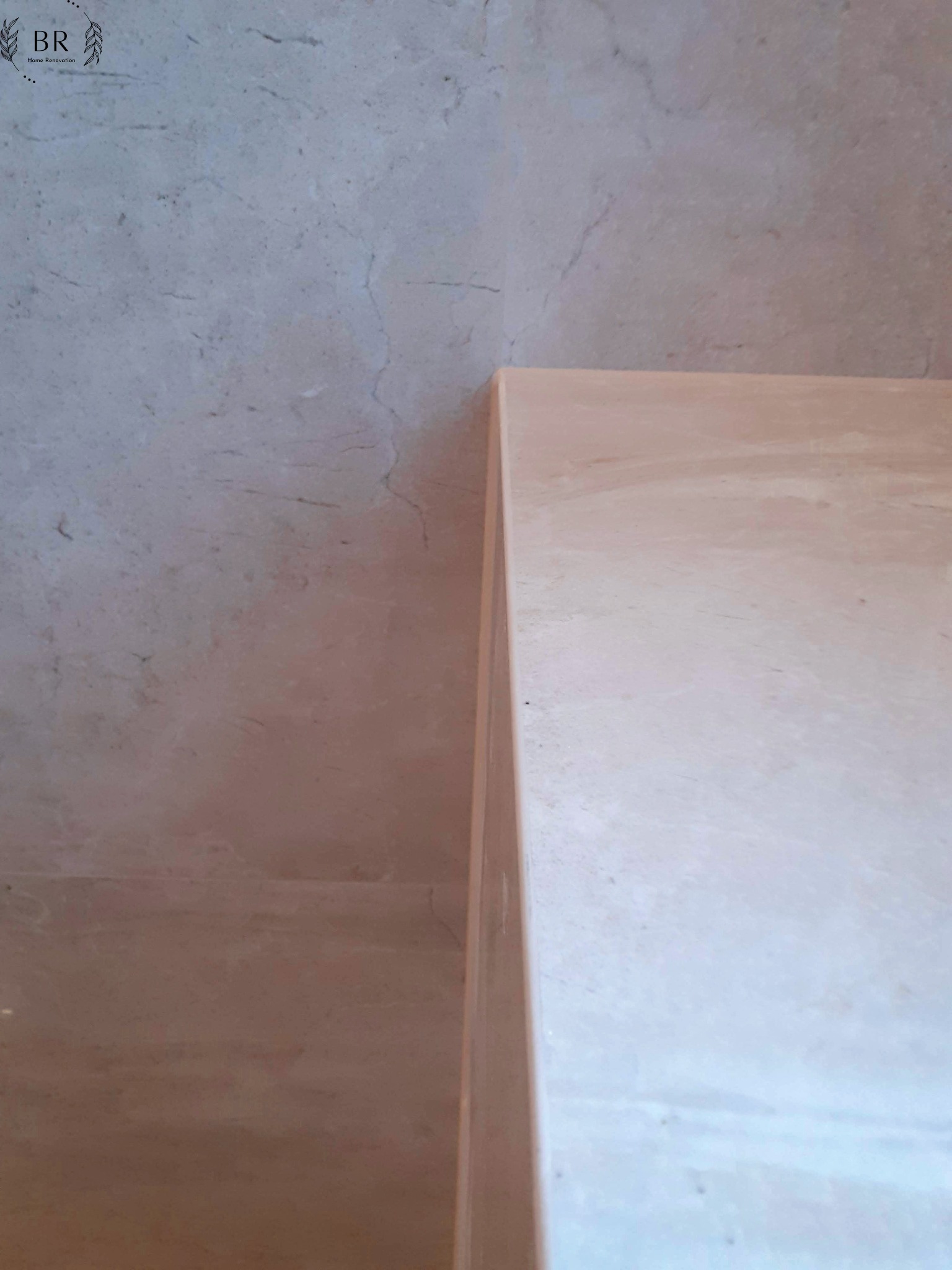 Fragment ściany i blatu z beżowego marmuru z widocznymi żyłami, oświetlenie z góry podkreśla fakturę materiału.