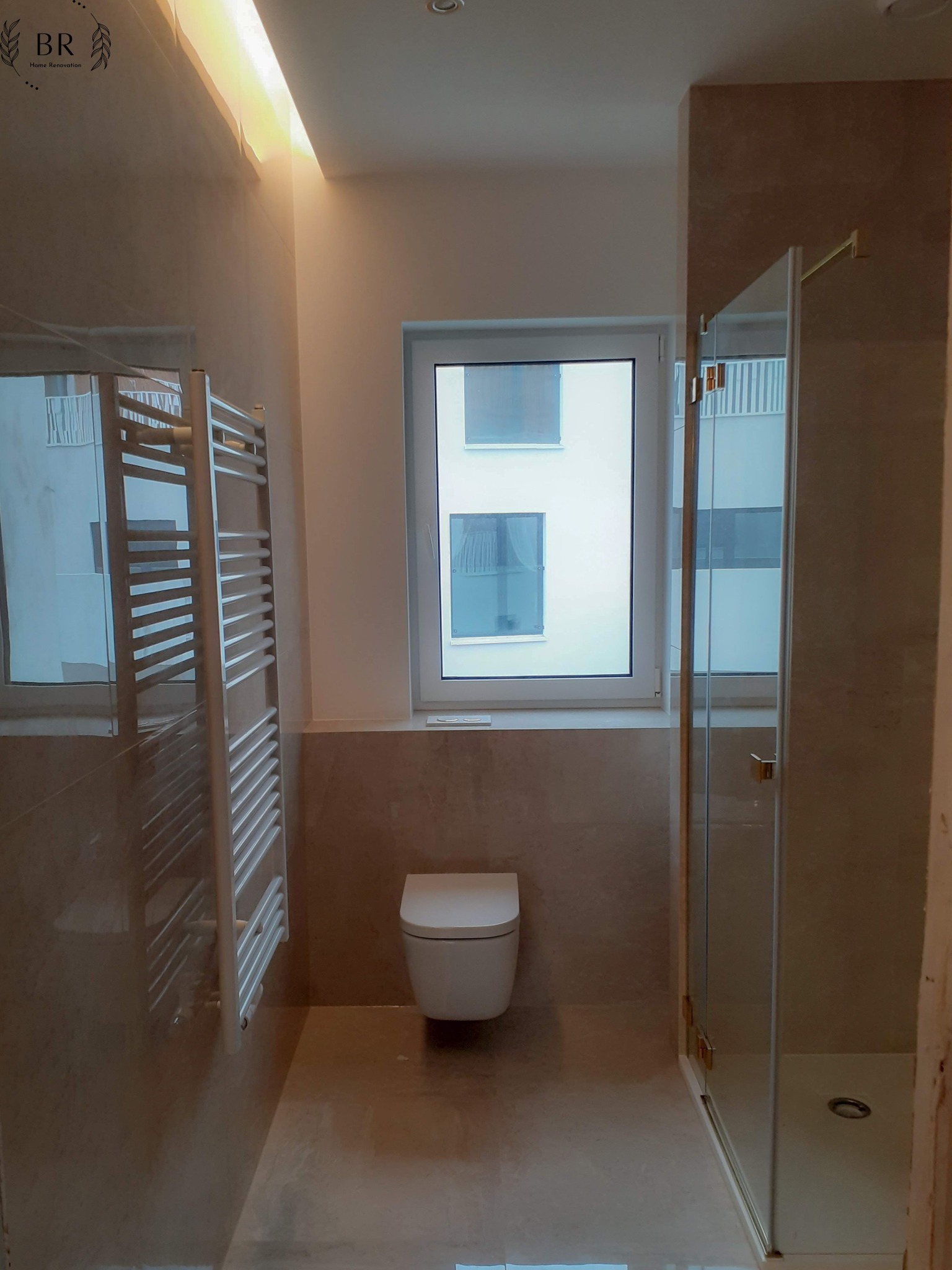 Ukończona łazienka z beżowymi płytkami, kabiną prysznicową ze złotymi okuciami, wiszącą toaletą i grzejnikiem drabinkowym, widok z perspektywy wejścia.