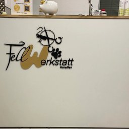 Fragola Creative Studio - Białe biurko z czarnym i złotym logo 'Fellwerkstatt Horaffen' z motywami zwierzęcymi i fryzjerskimi. Nad biurkiem skarbonka świnka i produkty.