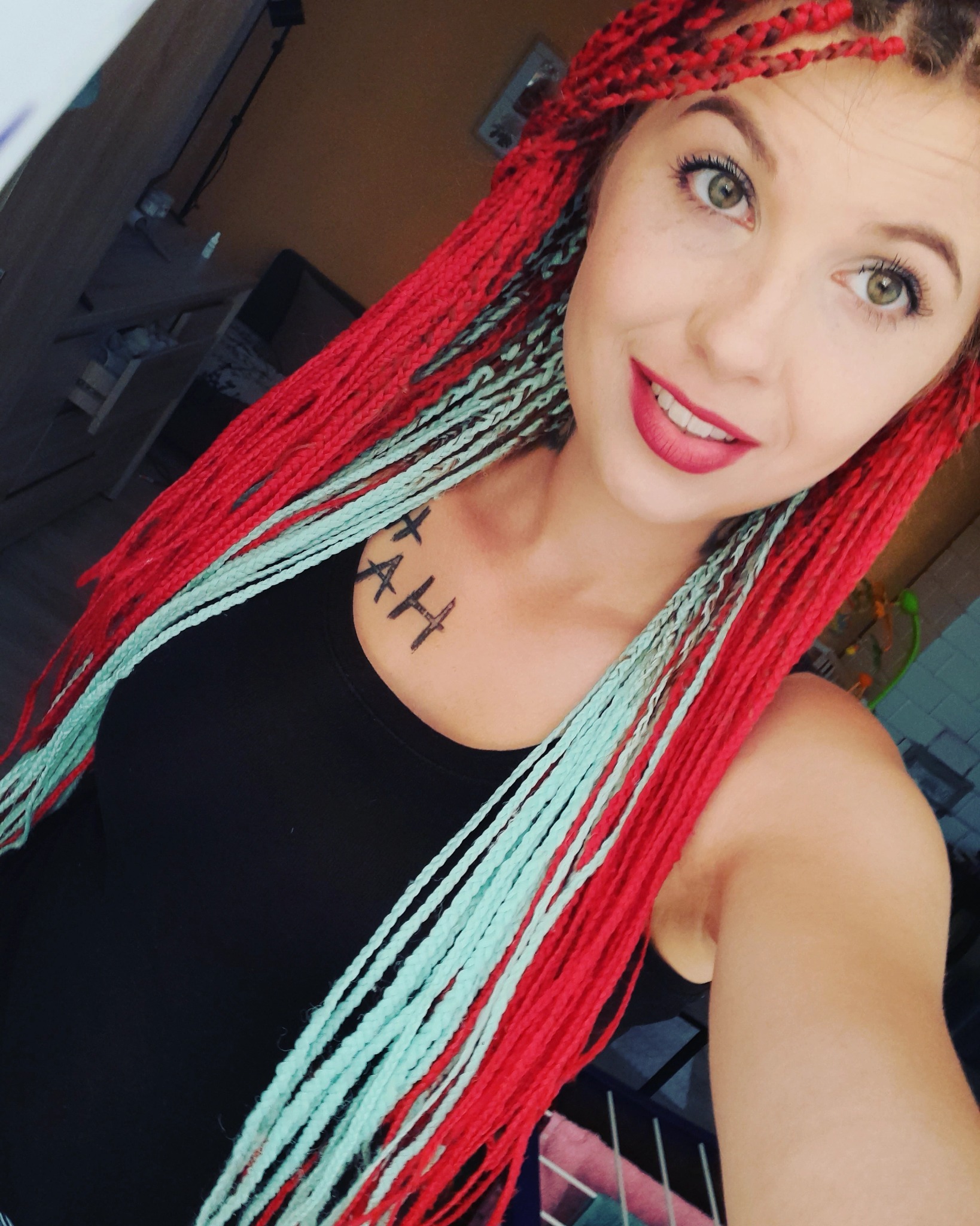 Uśmiechnięta kobieta z czerwono-turkusowymi warkoczykami bokserskimi i napisem na dekolcie.