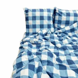 Pościel w niebiesko-białą kratę gingham, z widocznymi dwiema poduszkami, ułożona na łóżku z białym tłem.