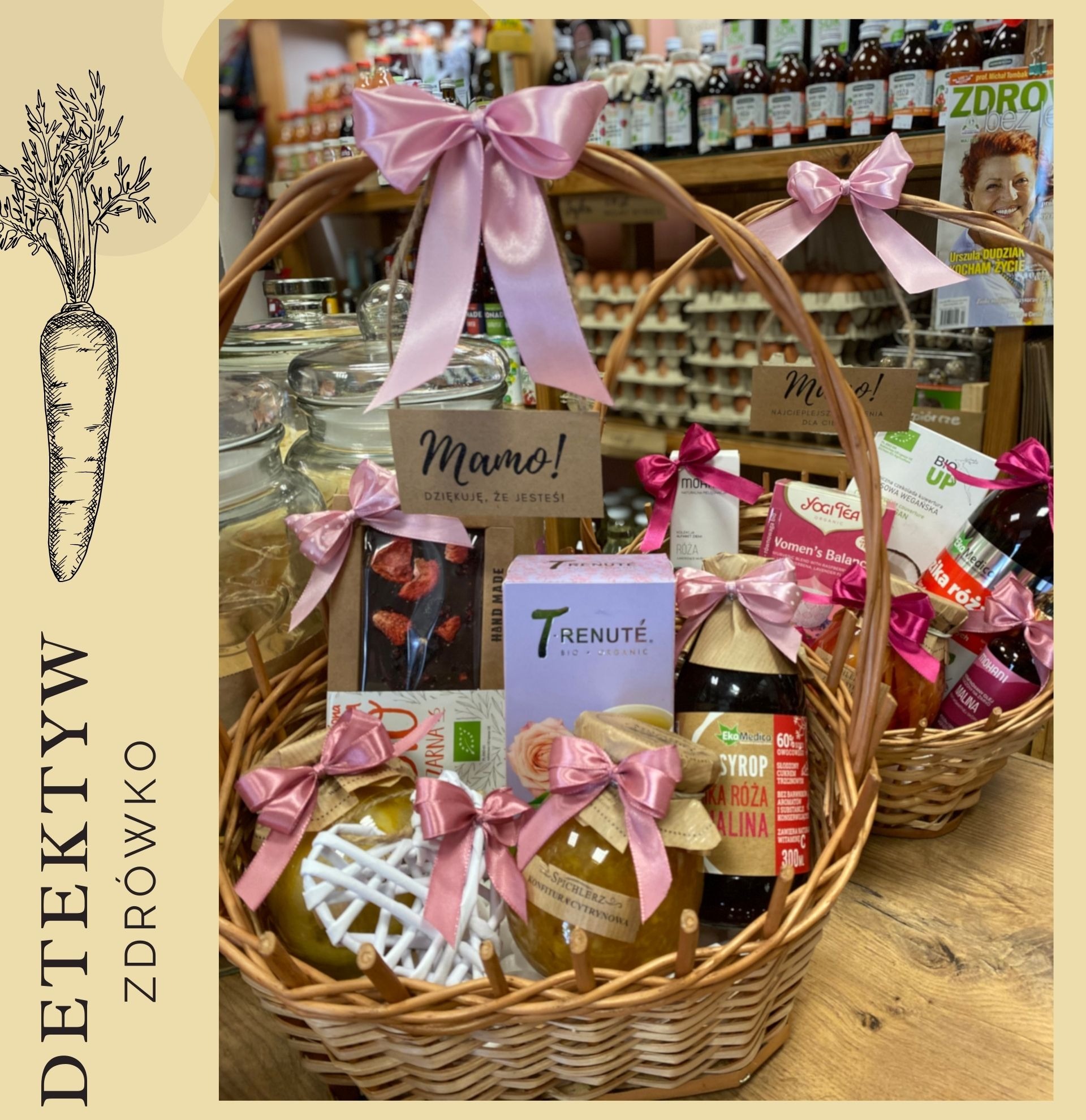 Kosz prezentowy wypełniony zdrową żywnością, w tym dżemami, syropami, herbatą i czekoladą, ozdobiony różowymi wstążkami, prezentowany w sklepie ze zdrową żywnością Detektyw Zdrówko.