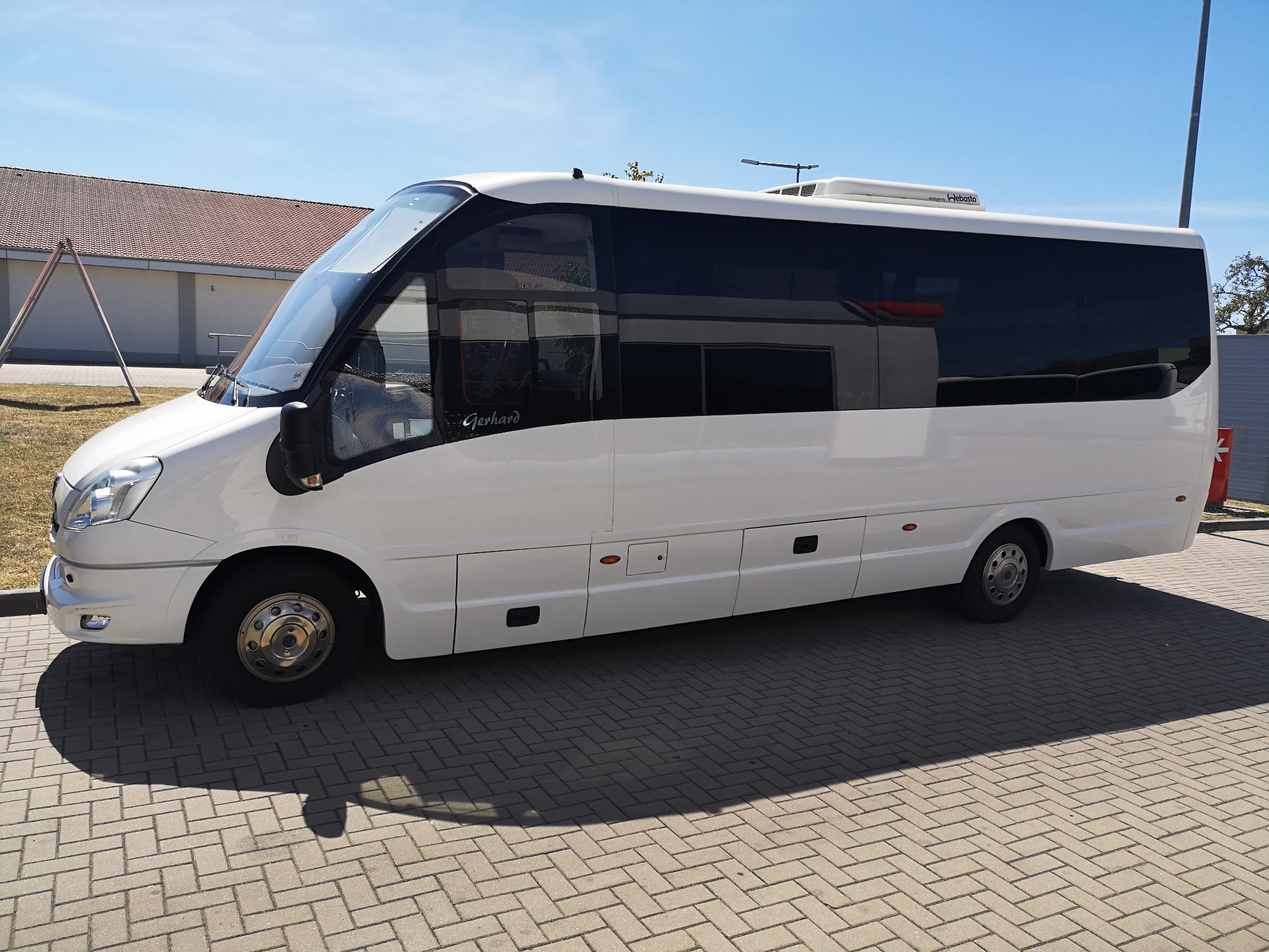 Biały bus z przyciemnianymi szybami marki Gerhard zaparkowany na brukowanej nawierzchni w słoneczny dzień.