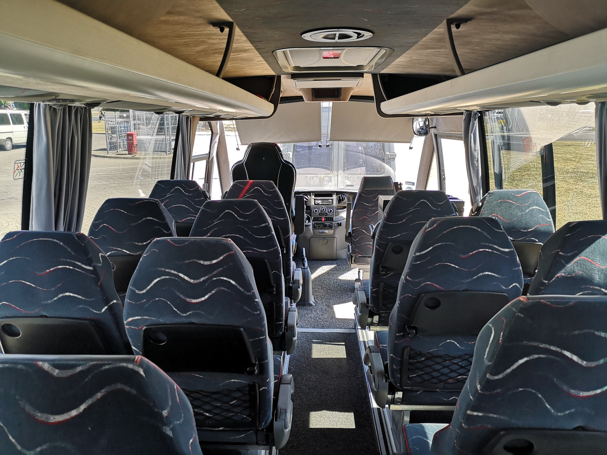 Wnętrze autobusu turystycznego z rzędami siedzeń z wzorem falistych linii, widok z tyłu w kierunku kabiny kierowcy i przedniej szyby.