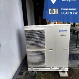 Zewnętrzna jednostka pompy ciepła Panasonic T-CAP 9 kW, zamontowana przy ścianie budynku na betonowych podstawach. Widoczne logo Panasonic oraz oznaczenie Inverter.