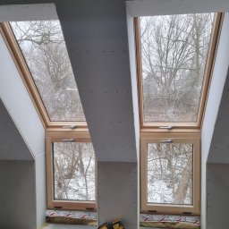 Wamas usługi remontowe budowlane - Poddasze z dwoma oknami dachowymi w trakcie montażu płyt kartonowo-gipsowych, widoczna wełna mineralna pod oknami i narzędzie do mocowania płyt.