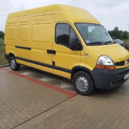 Żółty samochód dostawczy Renault Master zaparkowany na kostce brukowej w pochmurny dzień.