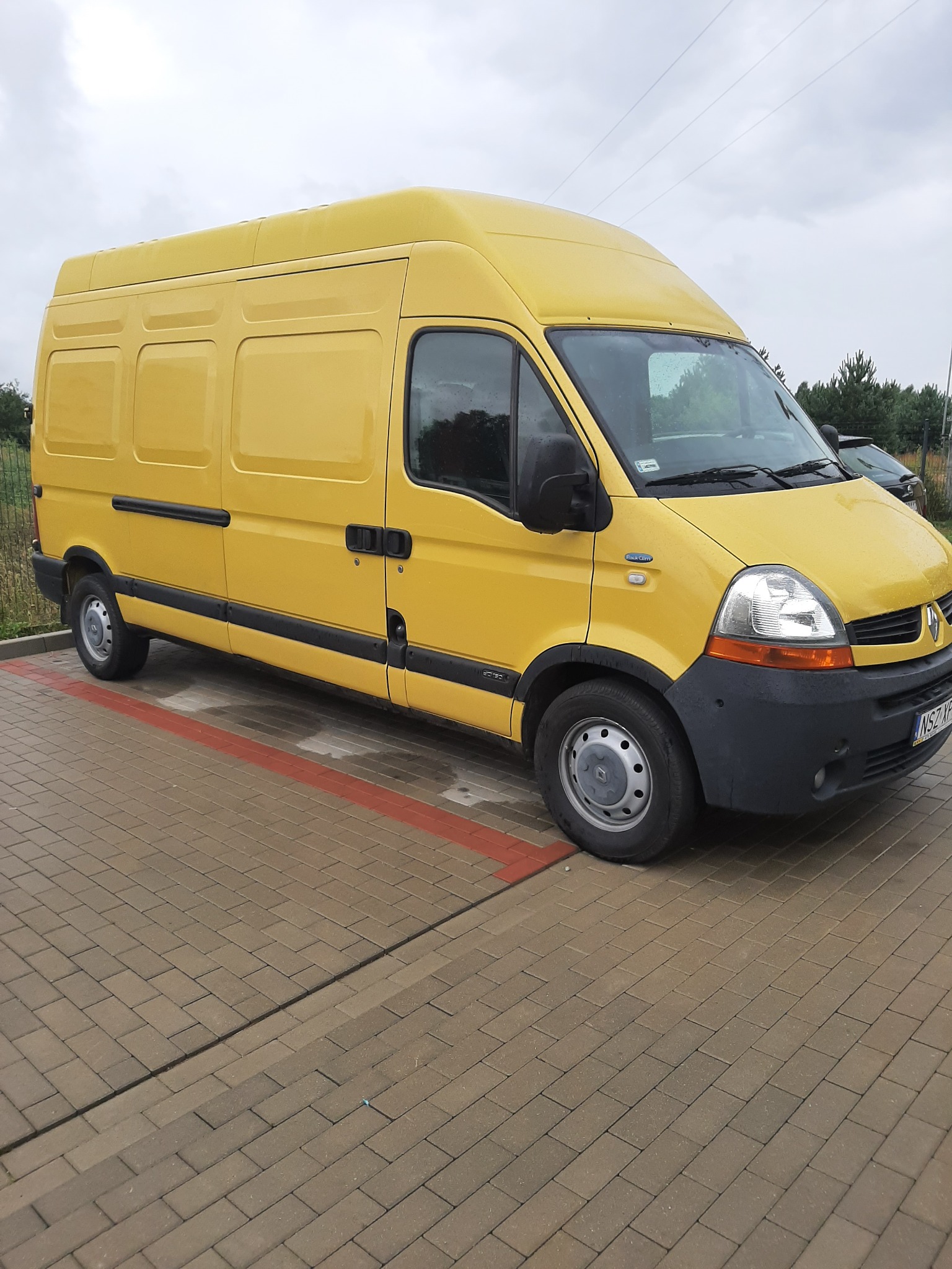 Żółty samochód dostawczy Renault Master zaparkowany na kostce brukowej w pochmurny dzień.