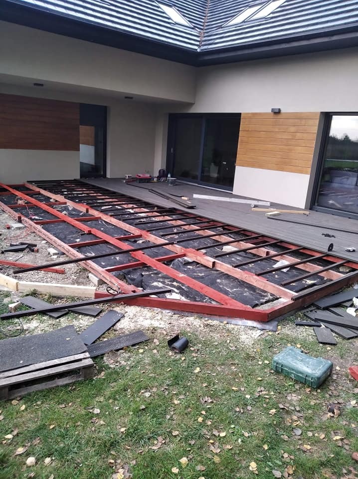 Konstrukcja pod taras kompozytowy na trawie, częściowo ułożone deski, widoczne elementy mocujące i skrzynka narzędziowa.