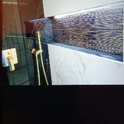 Nowoczesna łazienka z czarnymi i marmurowymi płytkami, złotą armaturą i wnęką z mozaiką podświetloną listwą LED.