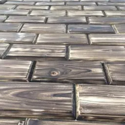 Drewniany taras z desek ułożonych w cegiełkę, z widocznym usłojeniem i delikatnymi wypaleniami na brzegach.