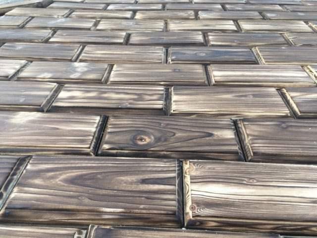 Drewniany taras z desek ułożonych w cegiełkę, z widocznym usłojeniem i delikatnymi wypaleniami na brzegach.