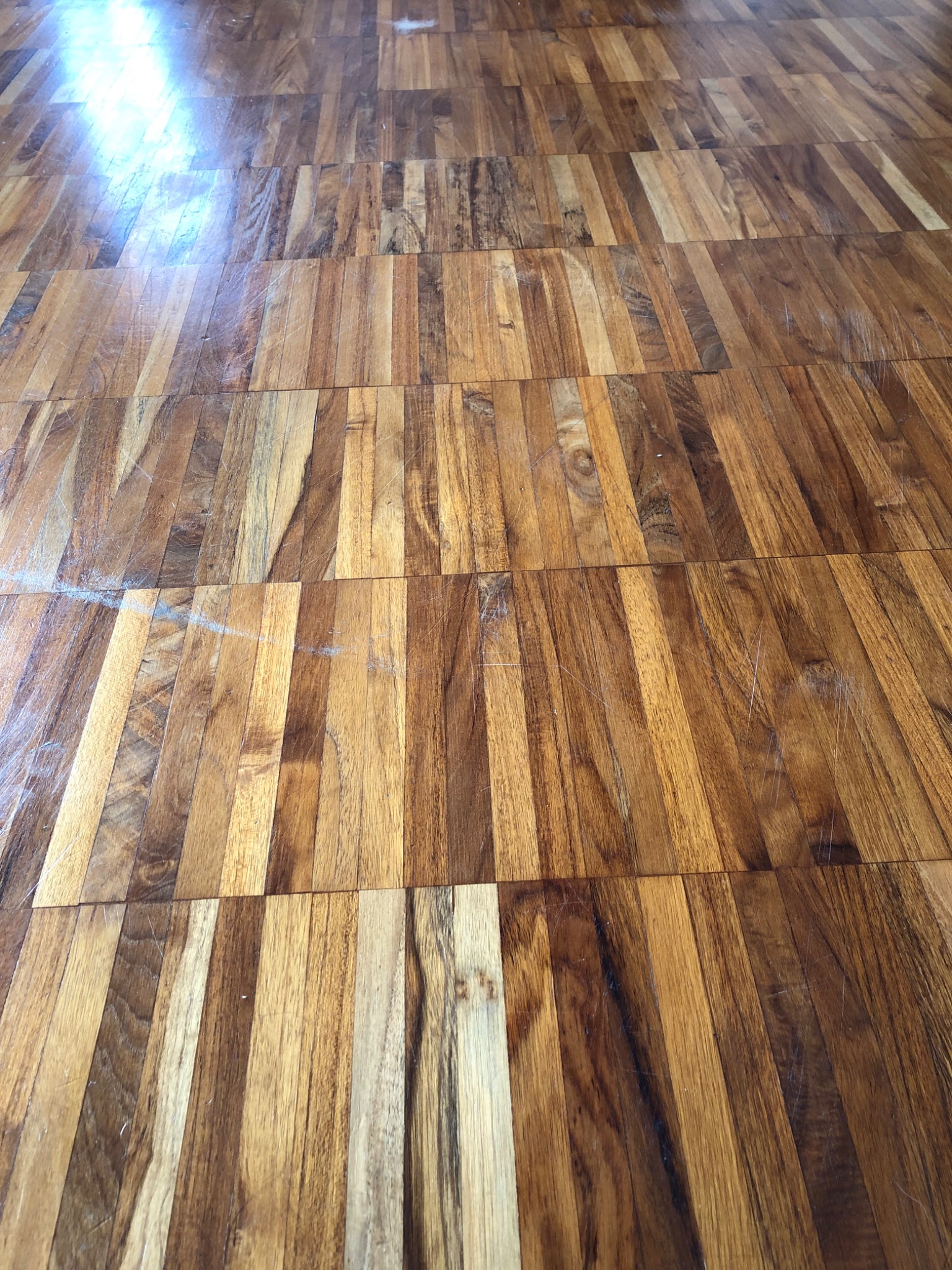 Parkiet z egzotycznego drewna w ciepłych odcieniach brązu i beżu, ułożony w regularny wzór z widocznymi drobnymi rysami i refleksami światła.