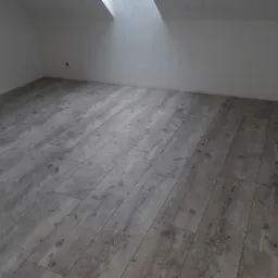 Nowo ułożony, szary parkiet laminowany w pustym pokoju na poddaszu z oknem dachowym.