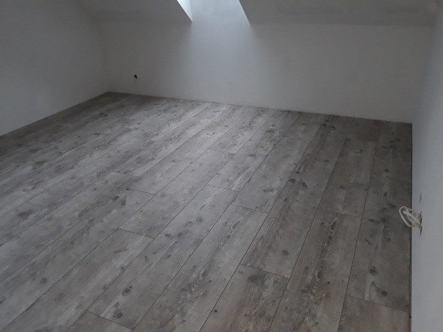 Nowo ułożony, szary parkiet laminowany w pustym pokoju na poddaszu z oknem dachowym.