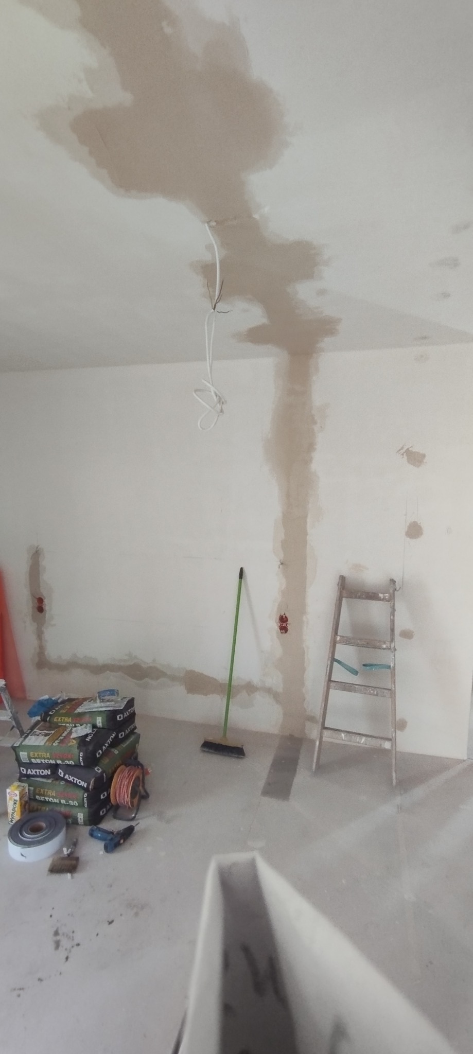 Przygotowanie ściany do nałożenia gładzi: widoczne ślady po szpachlowaniu na suficie i ścianach, drabina oparta o ścianę, worki z zaprawą Axton Beton R-30, przewody elektryczne wystające z sufitu...