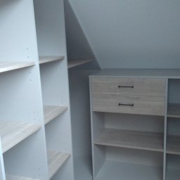 MABM Adam Bielawski - Szara szafa wnękowa z drewnianymi półkami i dwiema szufladami pod skosem dachu, widok z dołu na podłogę z paneli.