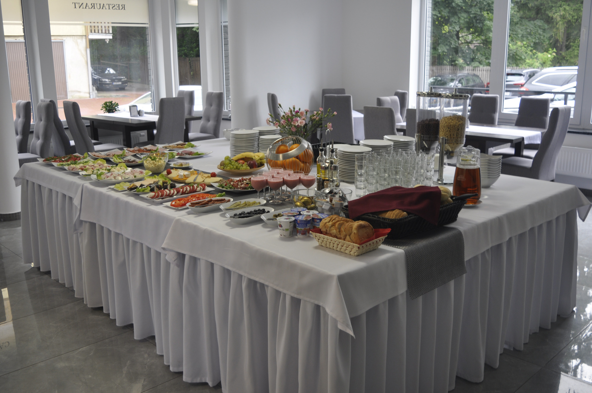 Stół bufetowy z różnorodnymi potrawami, napojami i dekoracjami w jasnym wnętrzu restauracji lub hotelu.