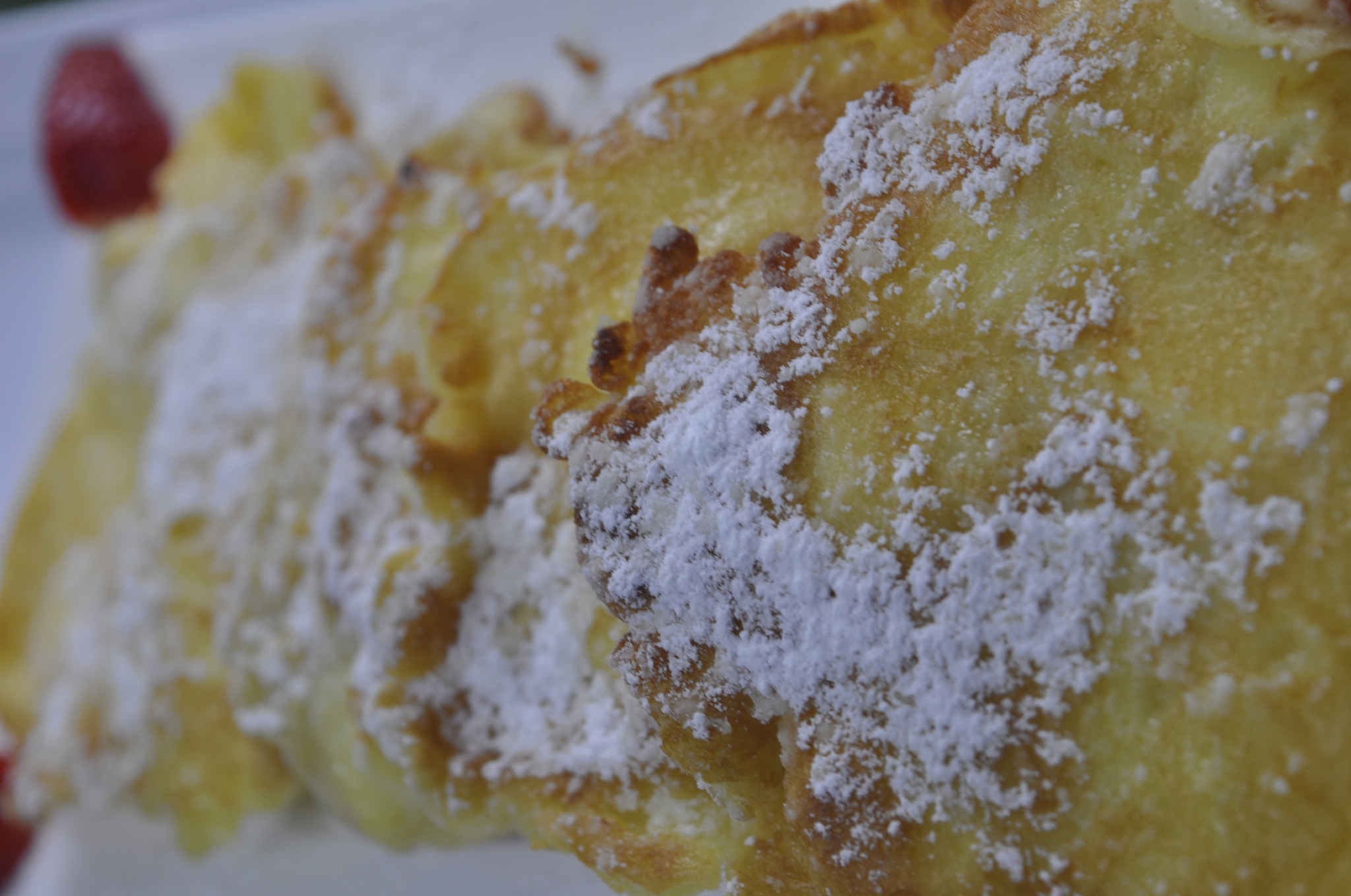 Bliski plan złotych tostów francuskich posypanych cukrem pudrem, z fragmentem truskawki w rogu.