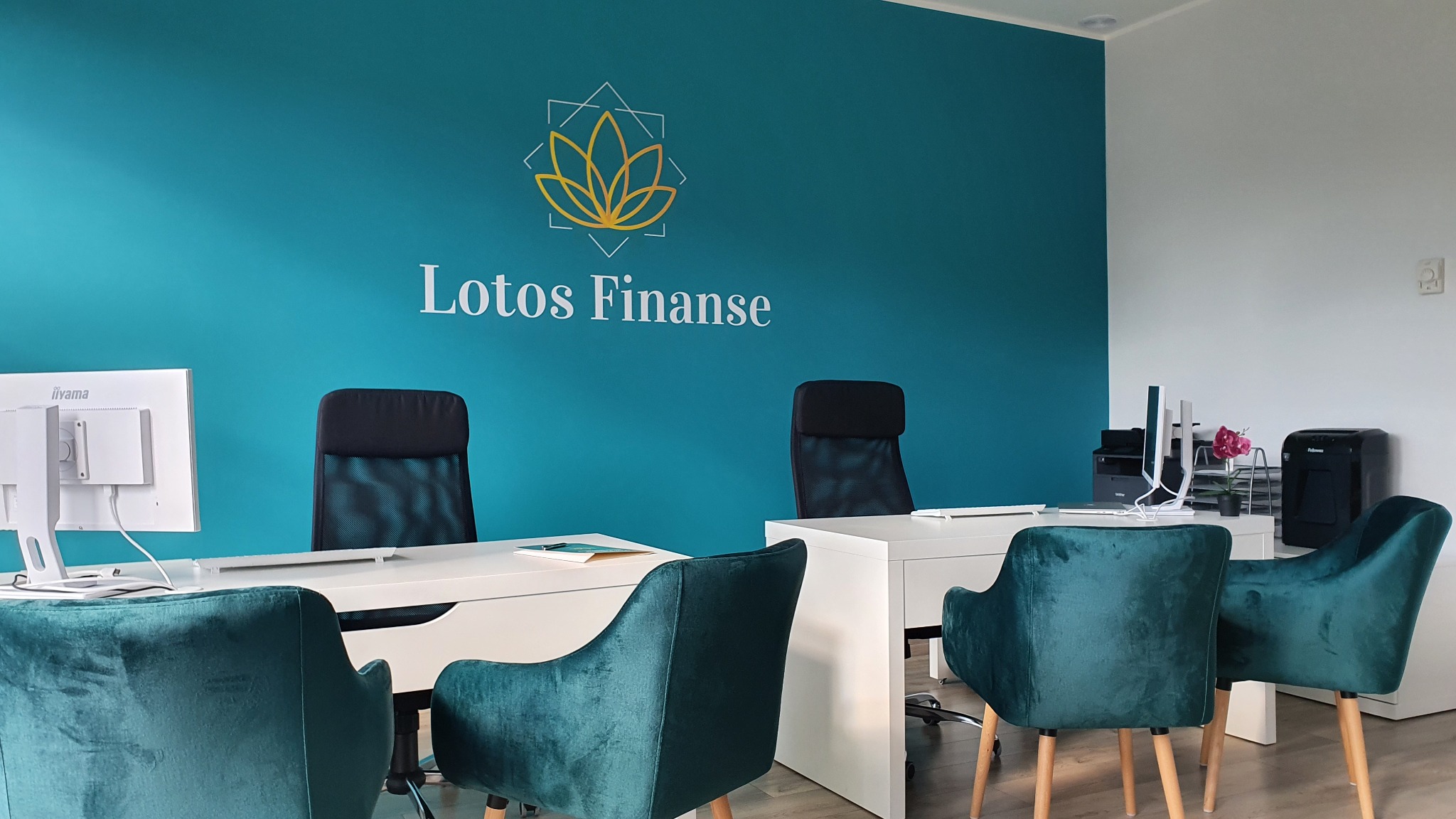 Biuro firmy Lotos Finanse z turkusową ścianą, logo z motywem kwiatowym, białymi biurkami i zielonymi krzesłami z weluru.