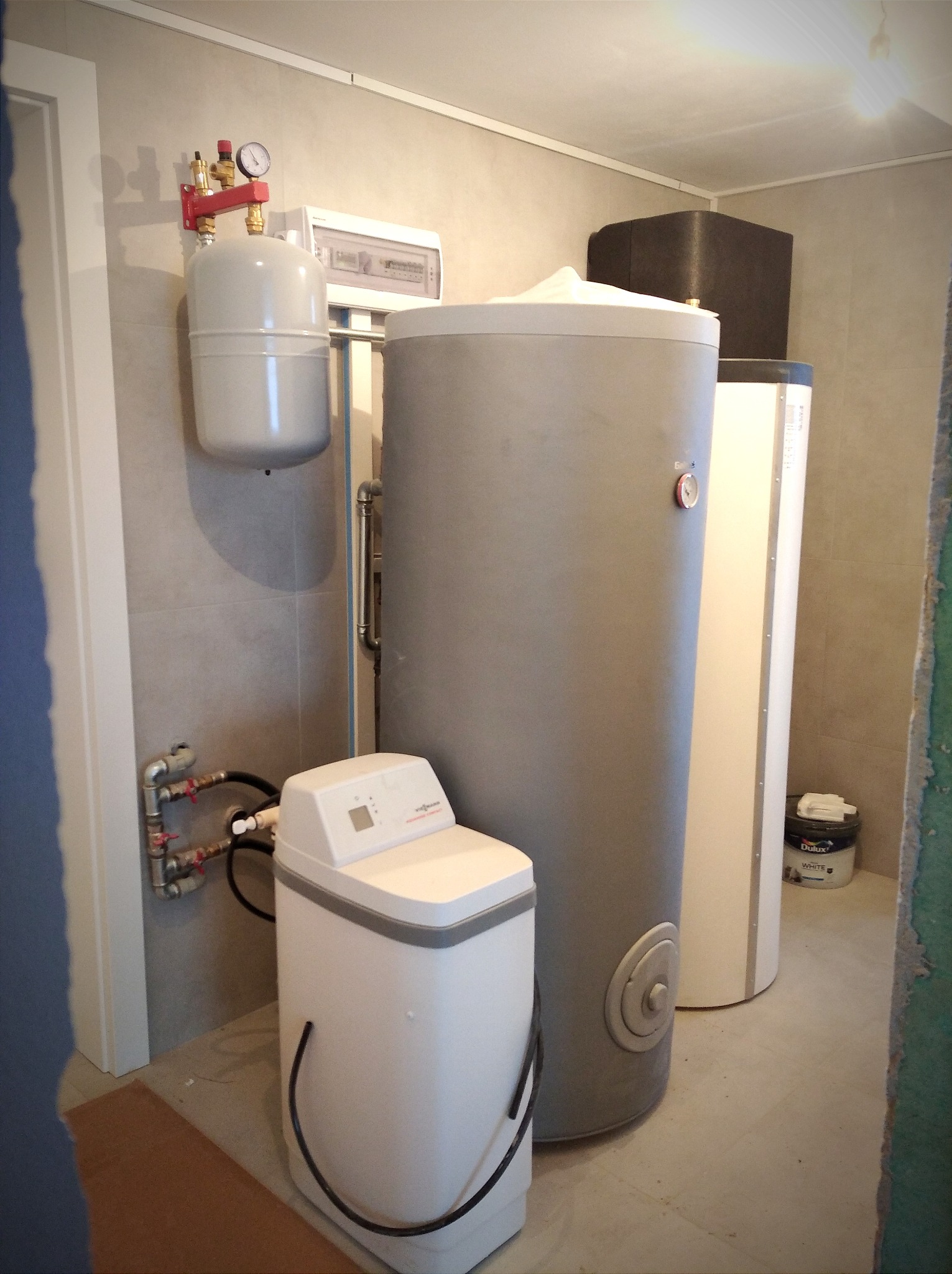 Kotłownia z zainstalowanym zasobnikiem ciepłej wody, zmiękczaczem wody i innymi elementami instalacji. Na ścianie widoczny manometr i zawory.