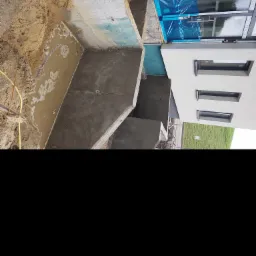 Betonowe fundamenty budynku w trakcie budowy, widoczna izolacja przeciwwilgociowa i częściowo zasypana ziemią przestrzeń fundamentowa.