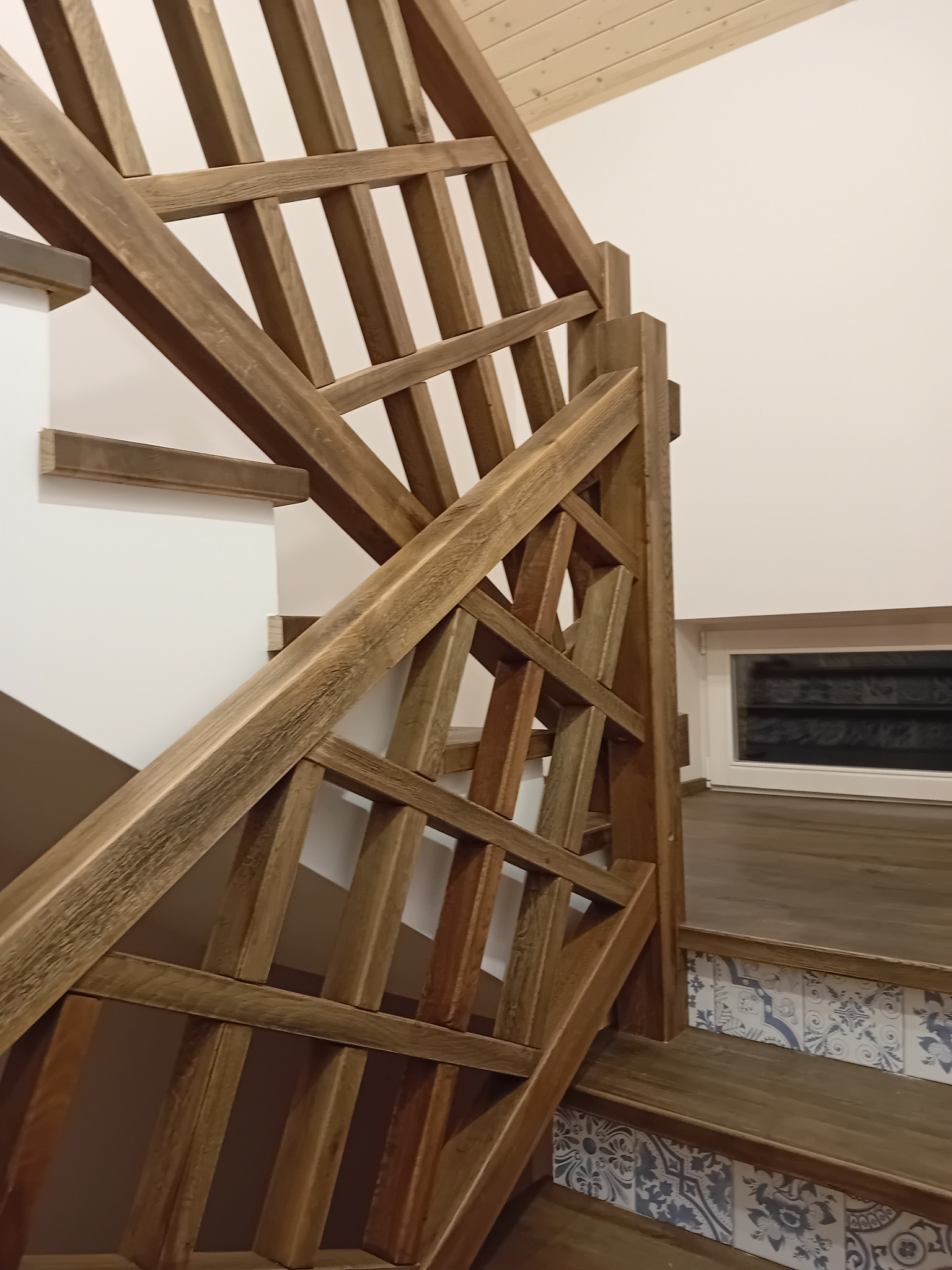 Drewniane schody z ozdobną balustradą i płytkami dekoracyjnymi na podstopnicach.