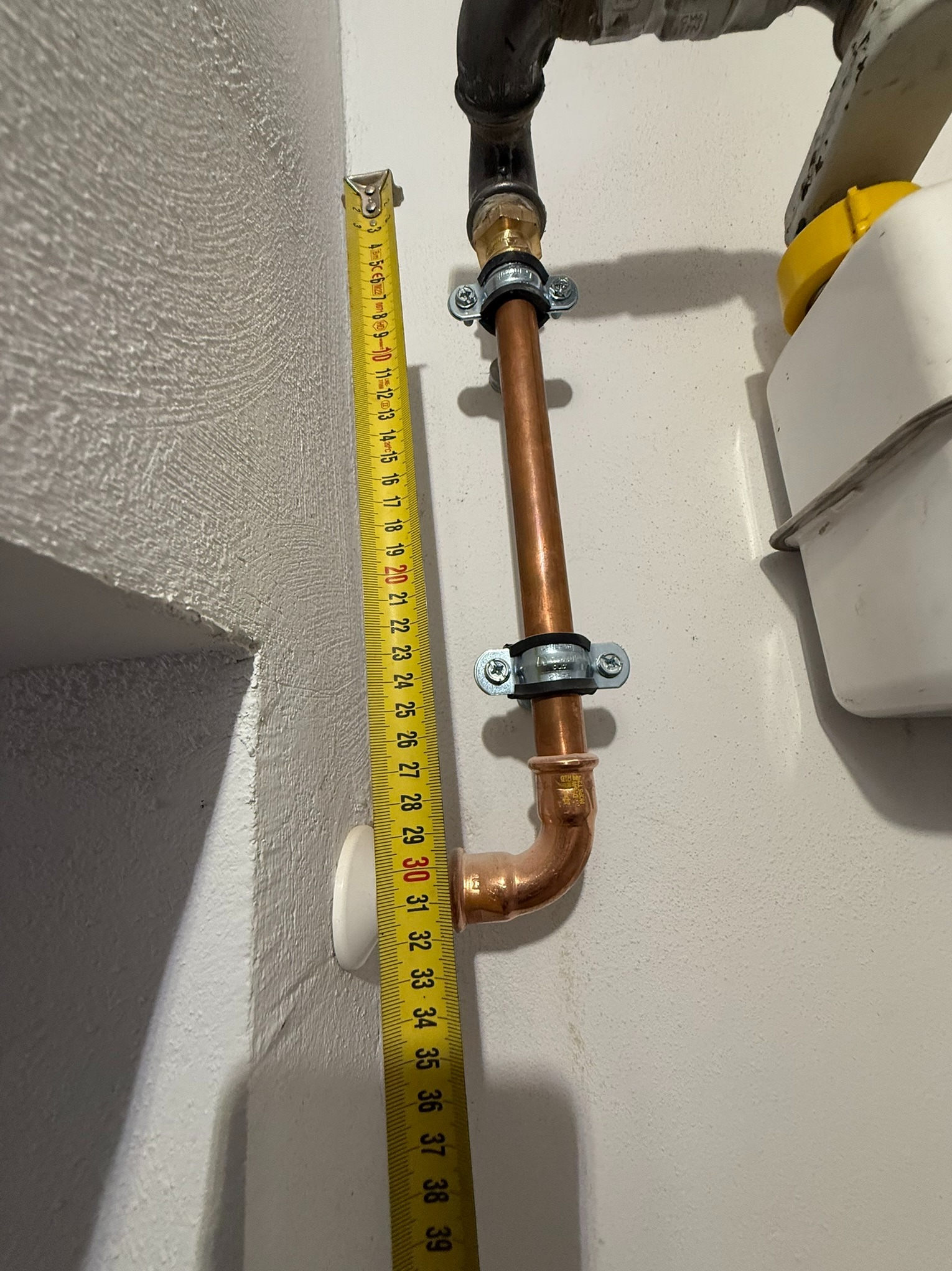 Miedziana instalacja gazowa z pomiarem odległości taśmą mierniczą w Radlinie. Widoczne mocowania rur i fragment gazomierza. Precyzyjny montaż instalacji.