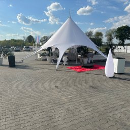 EVENT IMPERIUM - Biały namiot gwiazda na betonowym placu, otoczony meblami ogrodowymi i roślinami w donicach. Błękitne niebo z chmurami w tle. Słoneczny dzień.