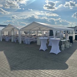EVENT IMPERIUM - Białe namioty z wyposażeniem na zewnątrz, przygotowane na imprezę plenerową. Widoczne stoły, krzesła i dekoracje. Słoneczny dzień, błękitne niebo z chmurami.