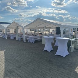 EVENT IMPERIUM - Ustawione białe namioty imprezowe z ławami i stołami na zewnątrz, dekoracje świecami i białe stoliki koktajlowe. Błękitne niebo z chmurami w tle.