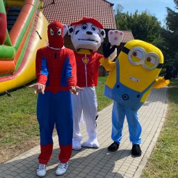EVENT IMPERIUM - Animatorzy w kostiumach: Spider-Man, Marshall z Psiego Patrolu i Minionek na tle dmuchanego zamku. Kostiumy z detalami, jasne oświetlenie, trawa i kostka brukowa.