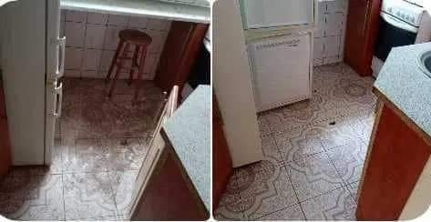 Kuchnia z zabrudzoną podłogą, widoczne plamy i zacieki na kafelkach, taboret w tle, wnętrze przed lub w trakcie porządkowania.