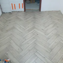 Ułożone panele podłogowe w jodełkę francuską z widocznymi śladami po remoncie i narzędziami w rogu pomieszczenia.